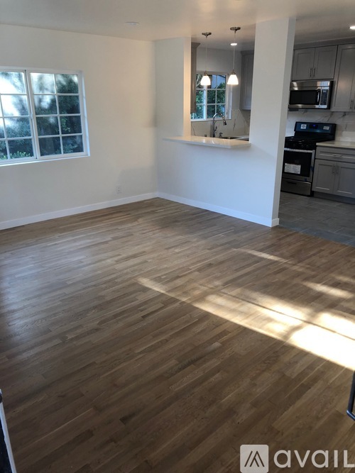 A room with wooden flooring and a kitchen area in the background.