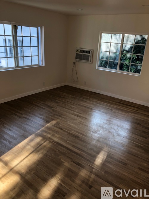 A room with wooden flooring and two windows.
