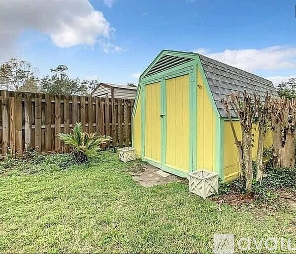 A small green and yellow shed sits in a grassy backyard.