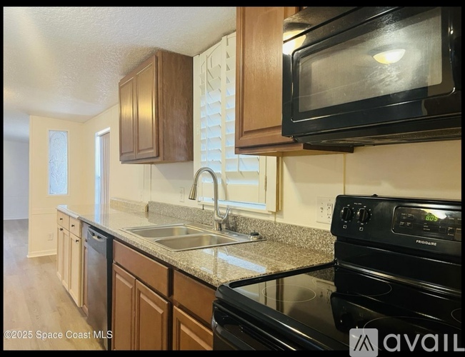 A kitchen with a black stove top oven and a black microwave above the sink.