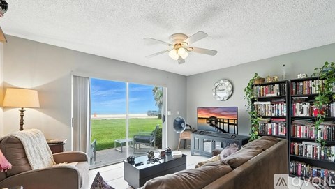 A living room with a brown couch, a fan, and a large window overlooking a green field.