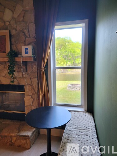 A living room with a stone fireplace and a table in front of a window.