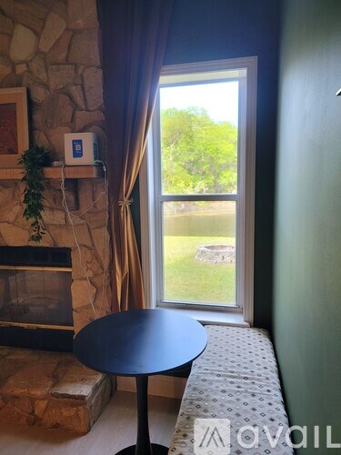 A living room with a stone fireplace and a table in front of a window.