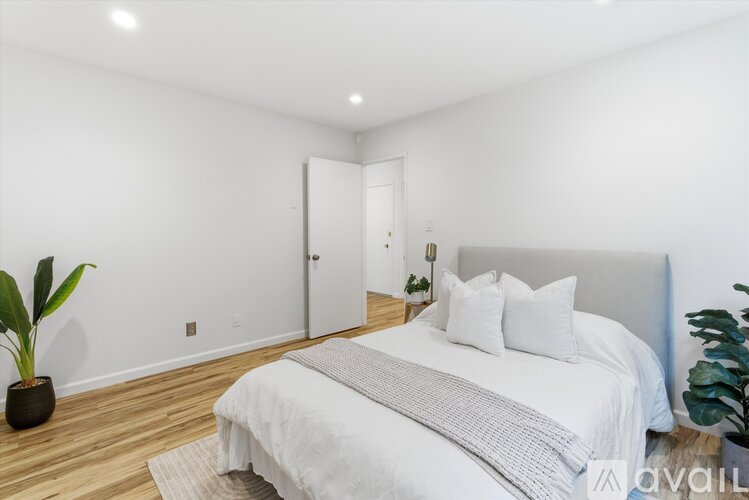 A bedroom with a large bed and a potted plant on the side table.