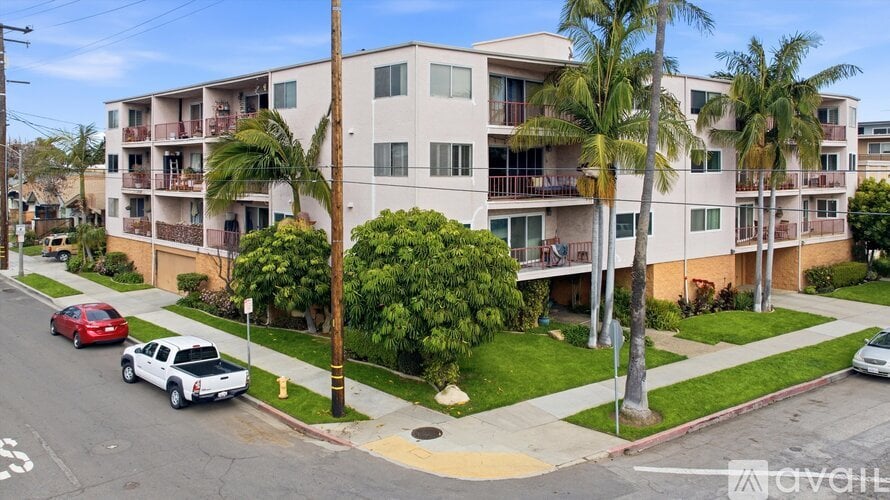 A street view of a residential area with apartment buildings, cars, and palm trees.