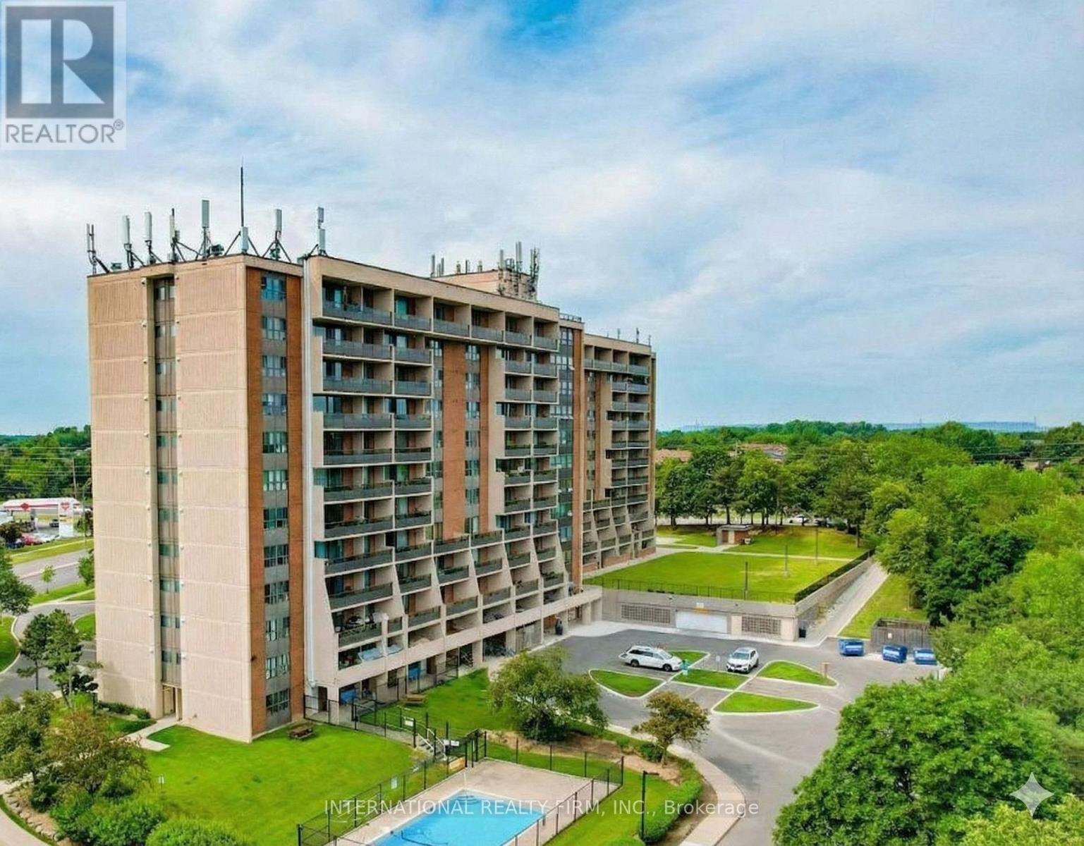 A large apartment building with a pool in the foreground and a grassy area in front.