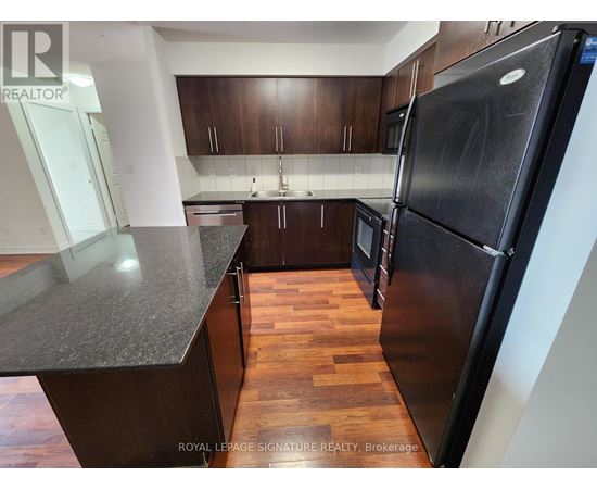 A kitchen with a black refrigerator and wooden floors.