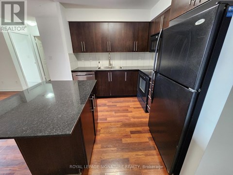 A kitchen with a black refrigerator and wooden floors.