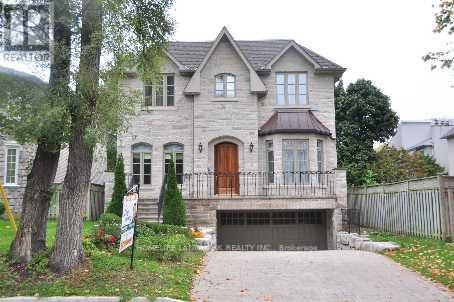 A large house with a garage is surrounded by a fence and trees.