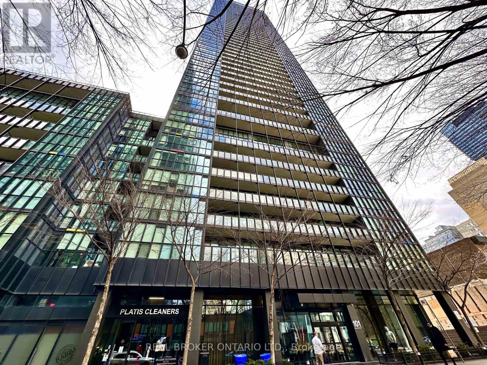 A tall building with a glass facade stands in front of a tree.