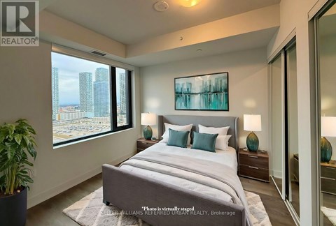 A bedroom with a large bed and a city view through the window.