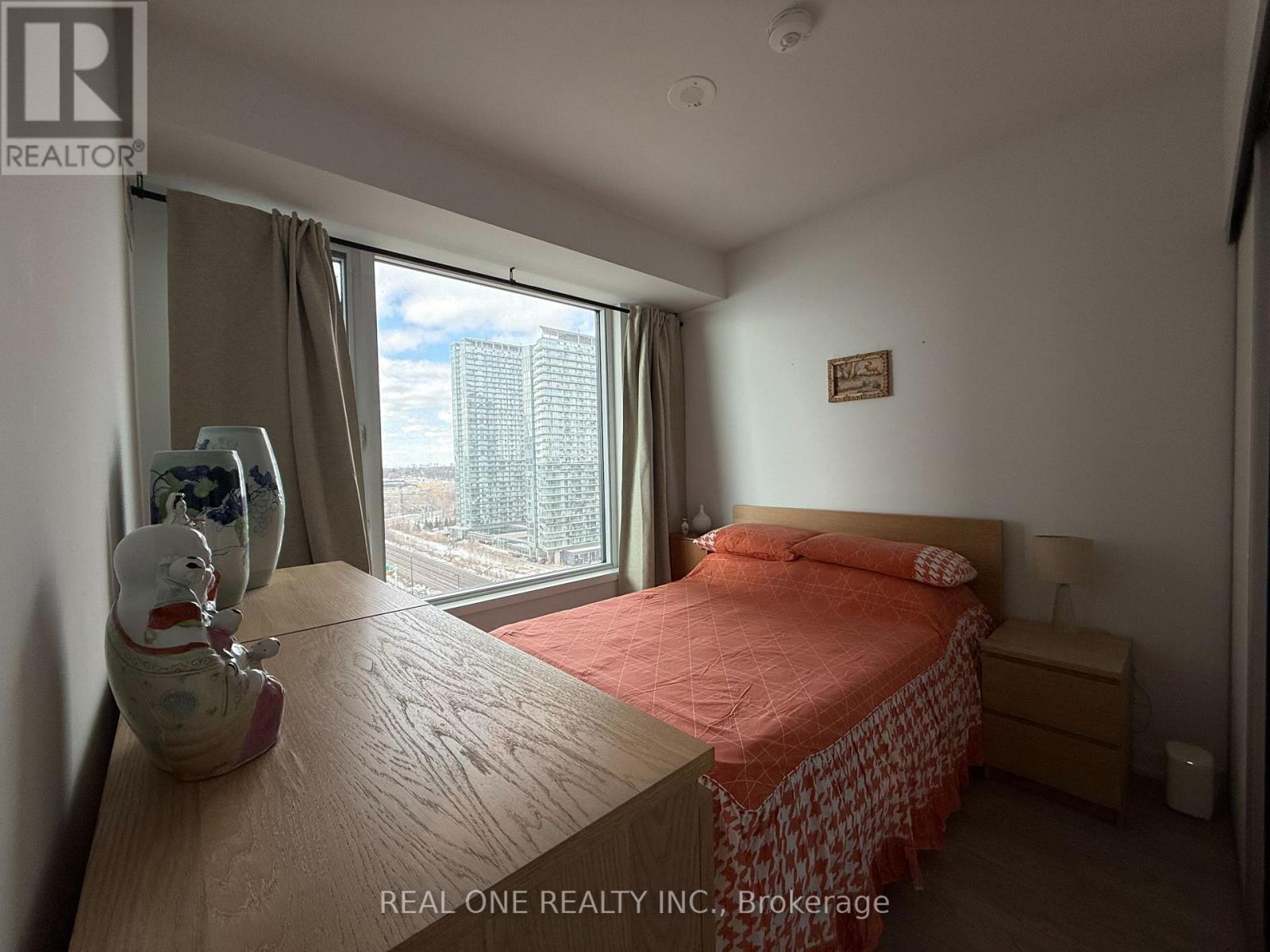 A bedroom with a bed, nightstand, and window overlooking a cityscape.