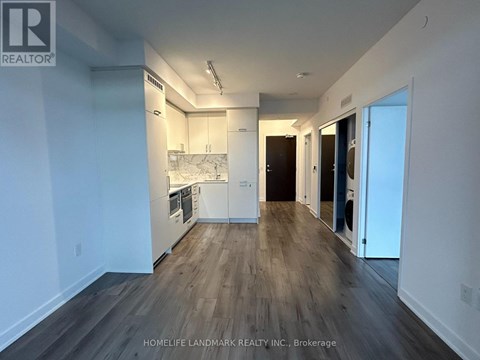 A spacious room with wooden flooring and white walls, featuring a kitchen area with a sink and a countertop.
