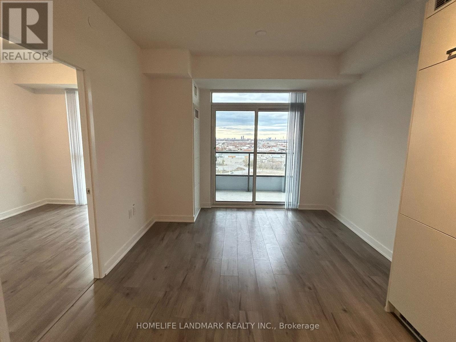 A spacious room with wooden flooring and a view of the city through the sliding glass door.