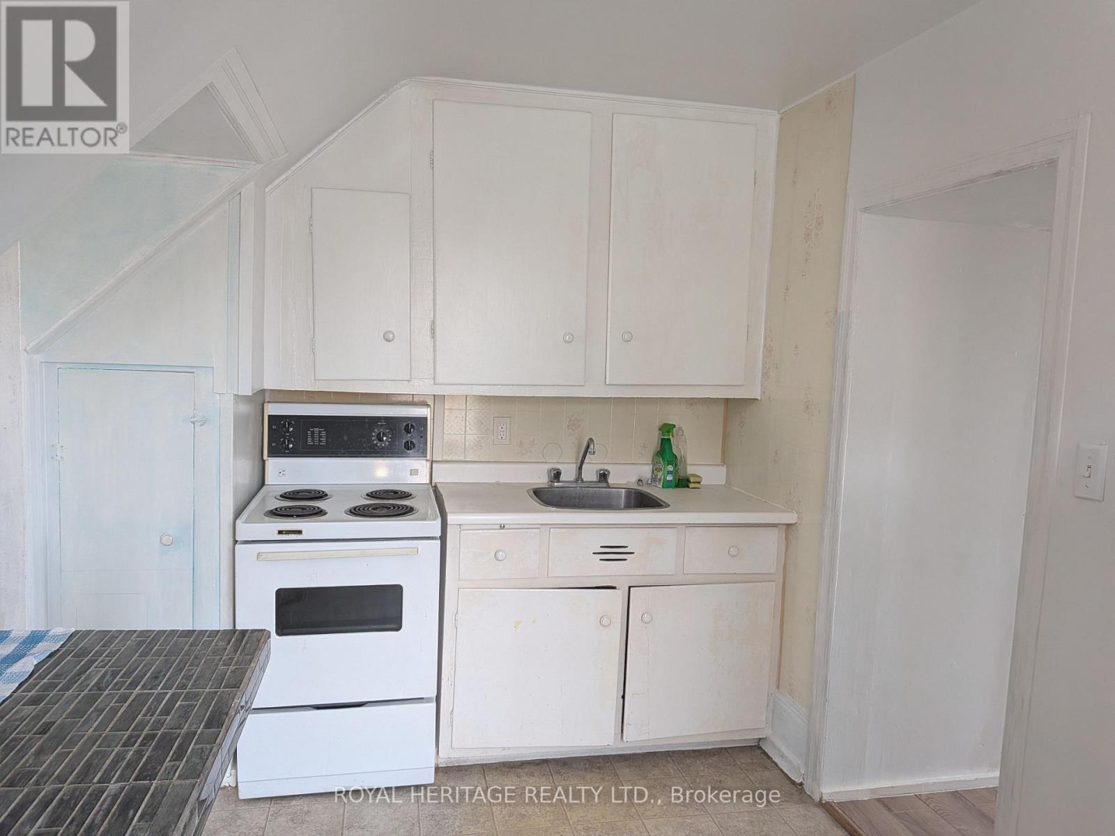 A white kitchen with a stove, sink, and cabinets.