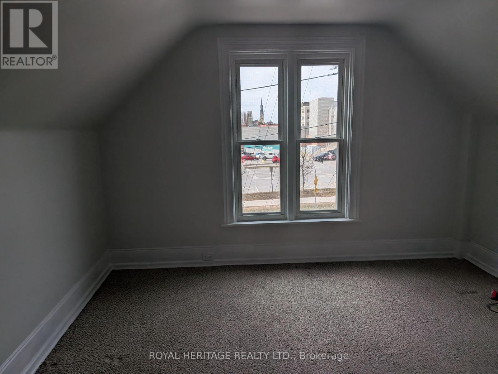 A room with a carpeted floor and a window showing a parking lot and buildings outside.
