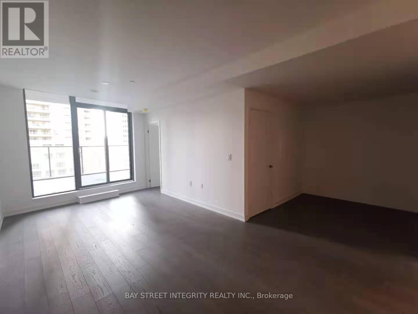 A spacious room with wooden flooring and large windows.