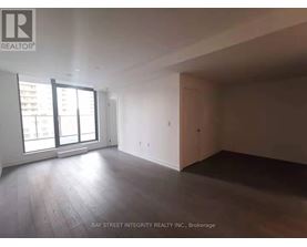 A spacious room with wooden flooring and large windows.