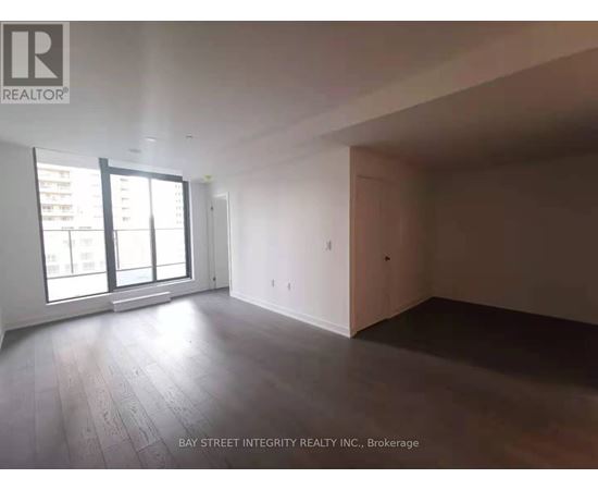 A spacious room with wooden flooring and large windows.