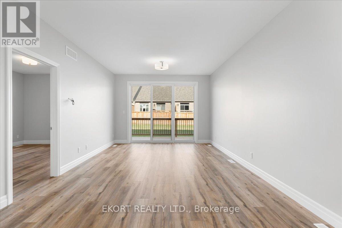 A spacious room with wooden flooring and white walls, with a view of a balcony through a glass door.