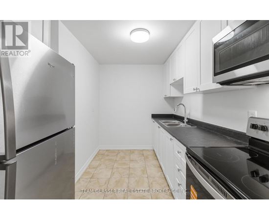 A kitchen with a stainless steel refrigerator and black countertops.