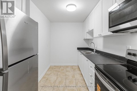 A kitchen with a stainless steel refrigerator and black countertops.