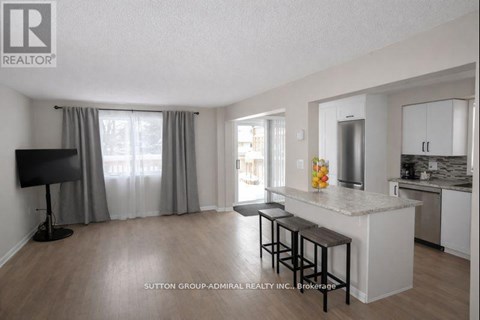 A living room with a television and a kitchen area in the background.