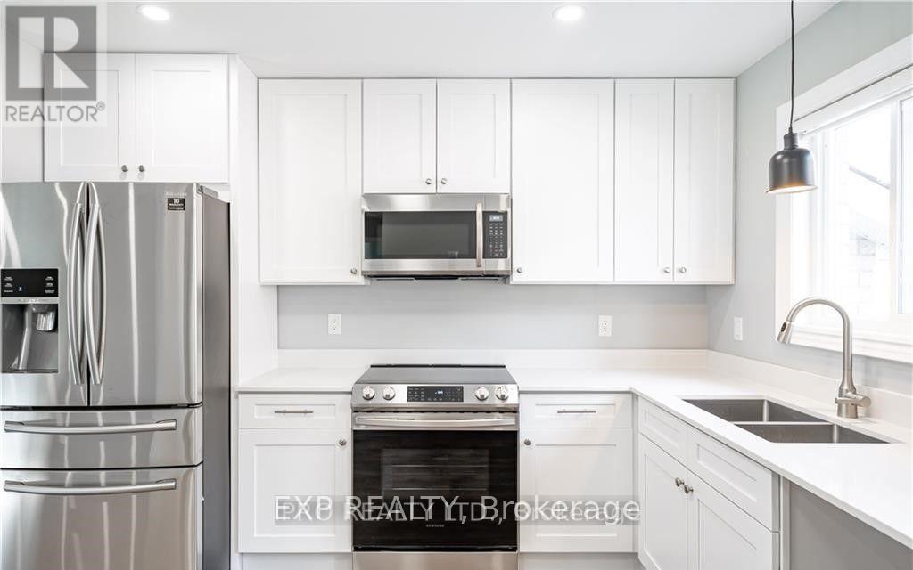 A white kitchen with a refrigerator, microwave, oven, and sink.