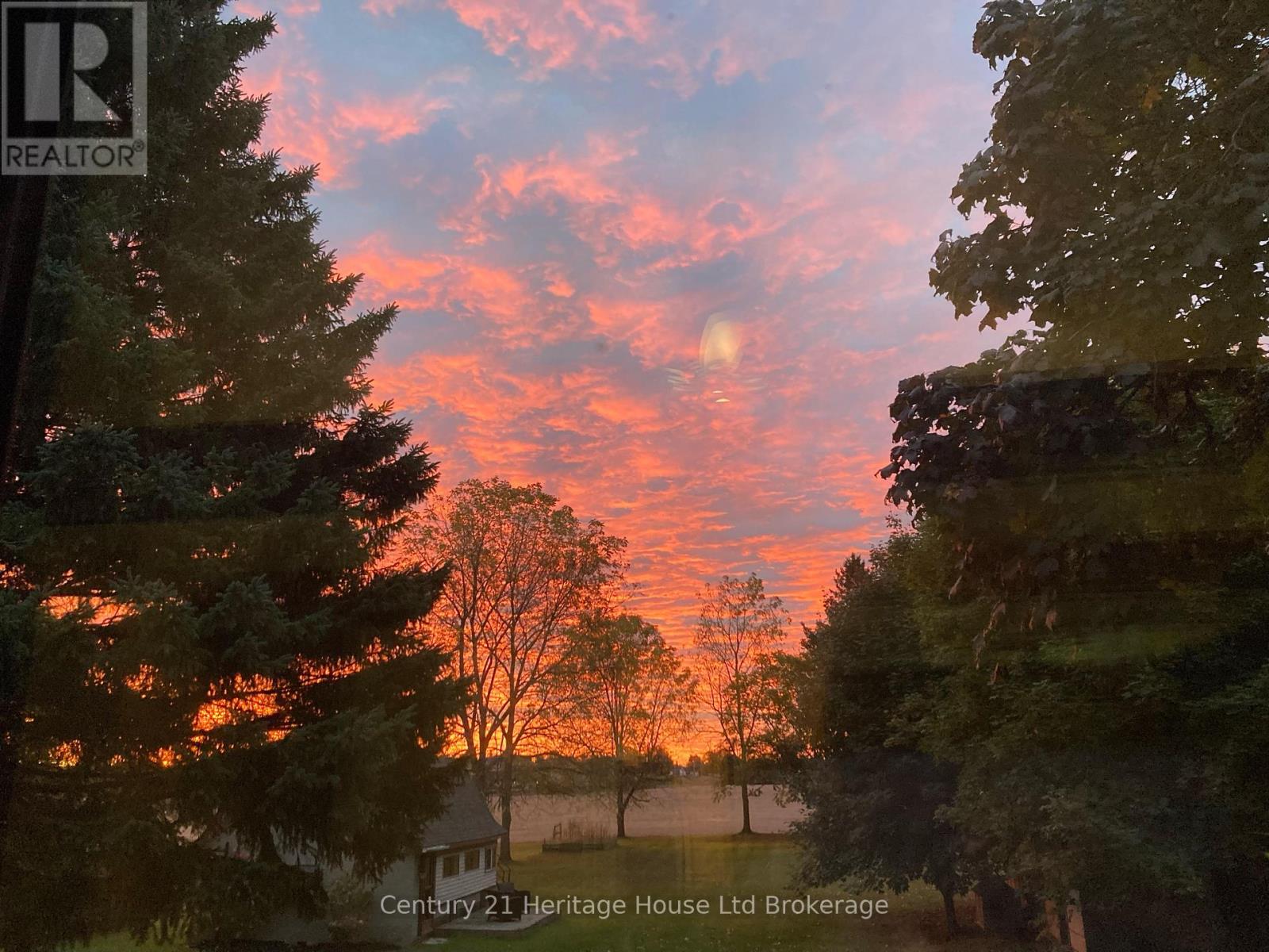 A beautiful sunset with a house and trees in the foreground.