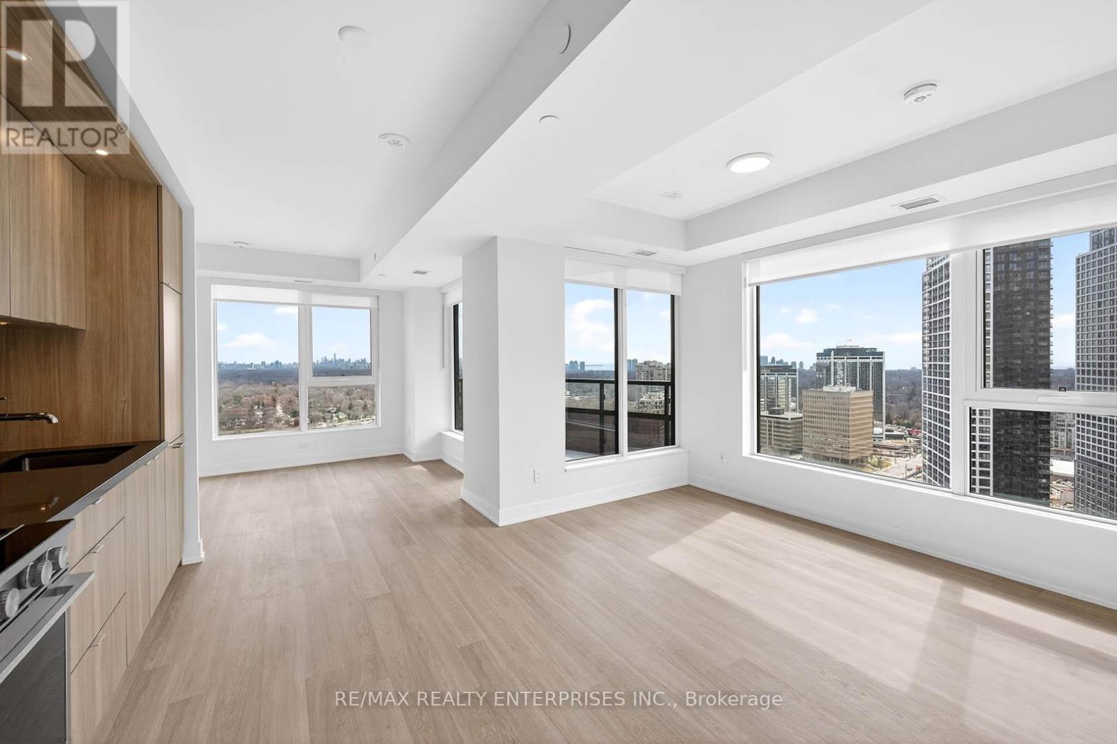 A spacious, well-lit room with wooden floors and large windows overlooking a cityscape.