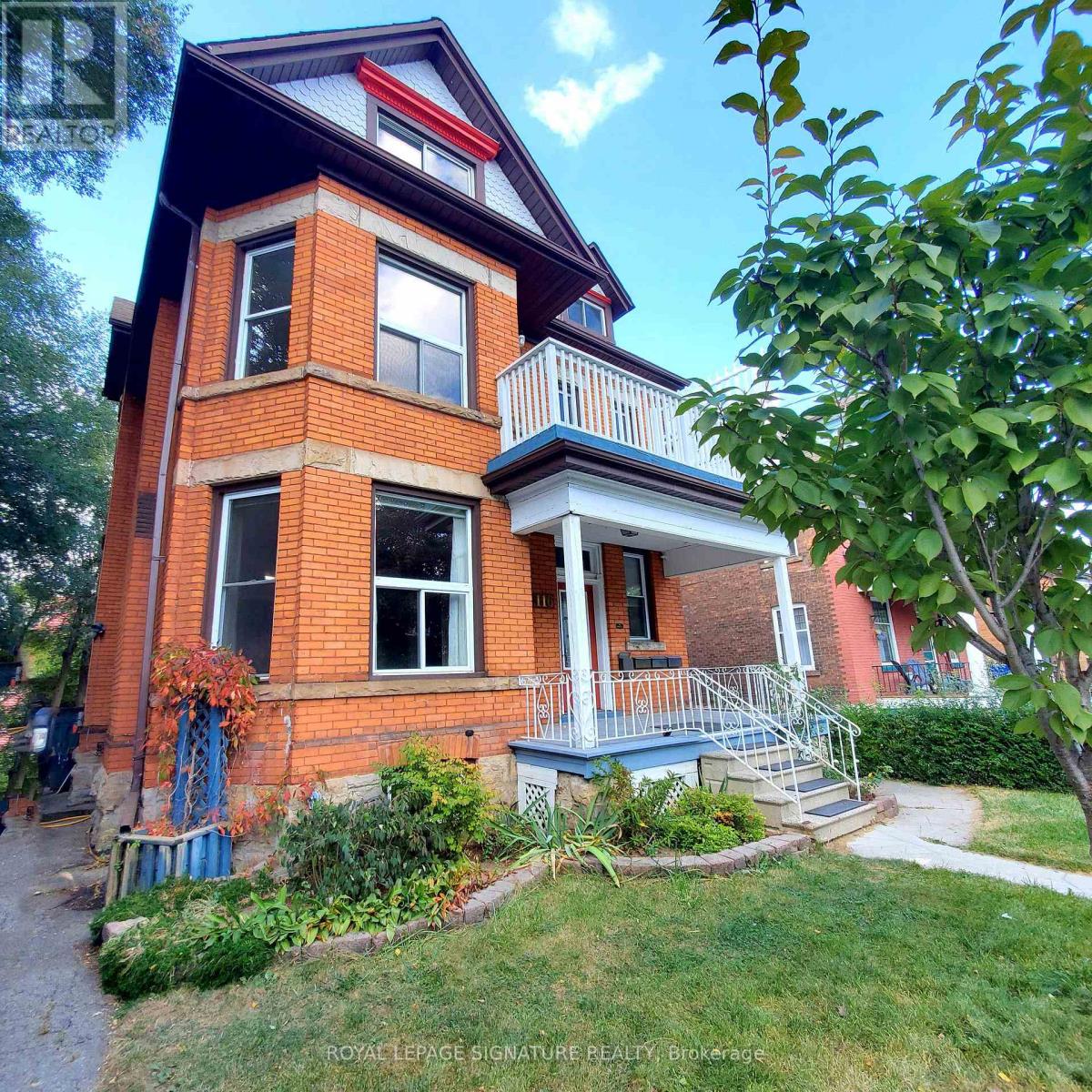 A red brick house with a balcony and a small garden in front.