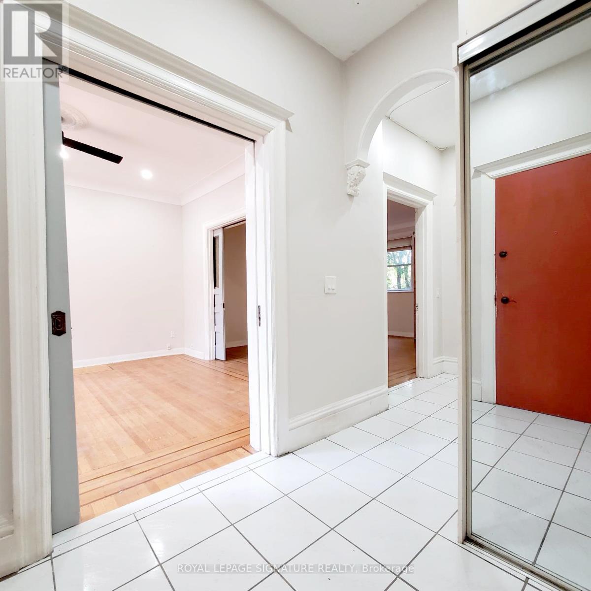 A white hallway with a red door and a white tiled floor.