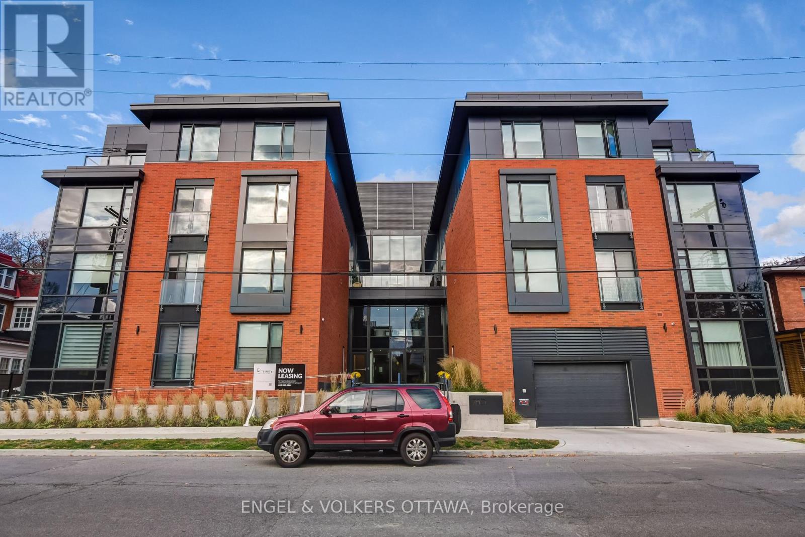 A red car is parked in front of a modern two-story building.