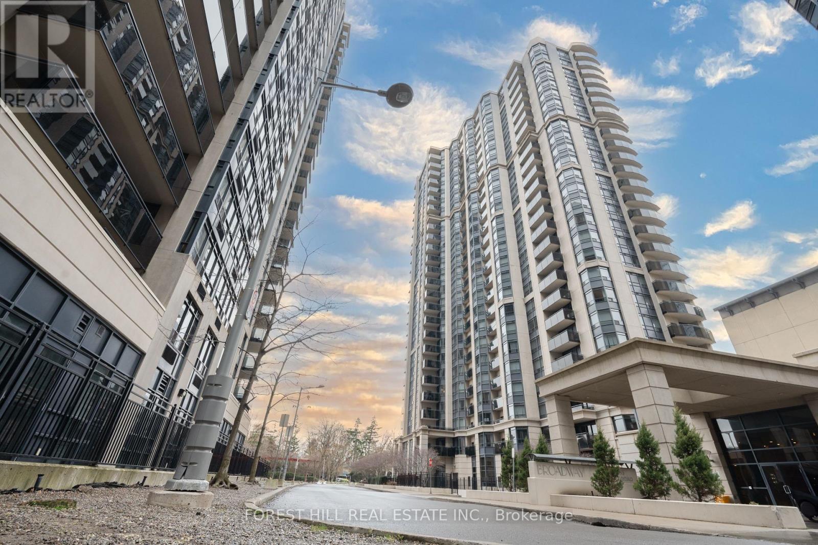 A tall residential building with a balcony and a tree in front of it.