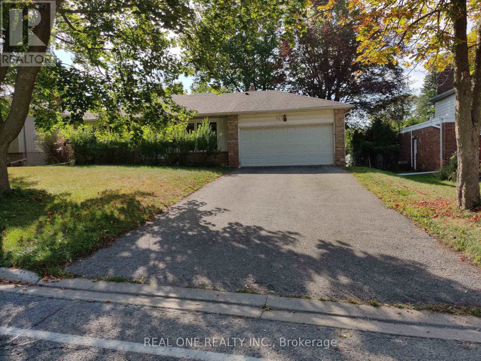 A driveway leads to a garage with a sign that says "REAL ONE REALTY INC., Brokerage.".