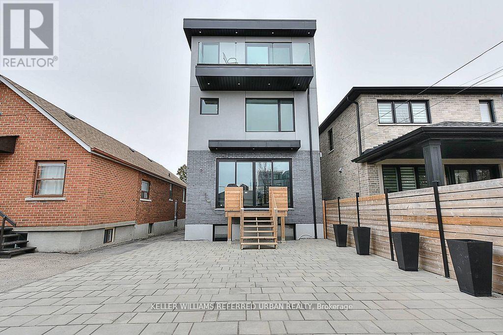 A modern two-story building with a balcony and a wooden door is surrounded by a brick wall and a wooden fence.