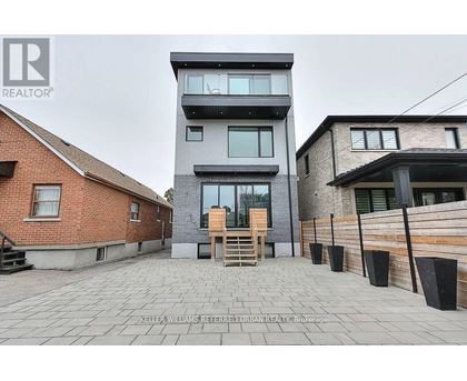 A modern two-story building with a balcony and a wooden door is surrounded by a brick wall and a wooden fence.