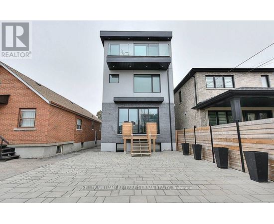 A modern two-story building with a balcony and a wooden door is surrounded by a brick wall and a wooden fence.