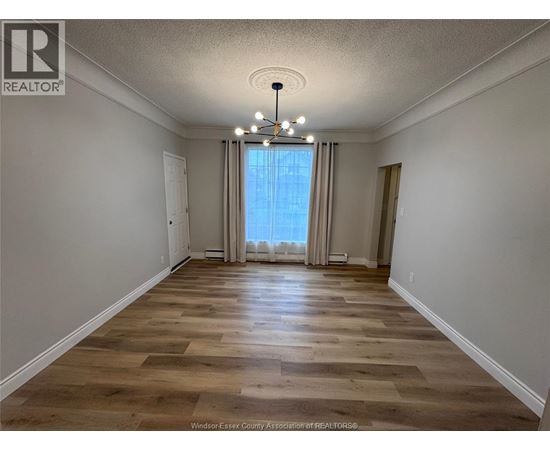 A room with wooden flooring and a large window with curtains.