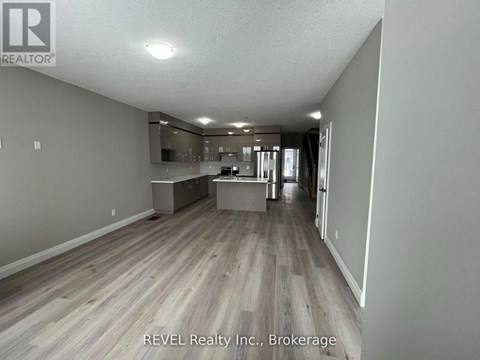A spacious room with wooden flooring and a kitchen area in the background.