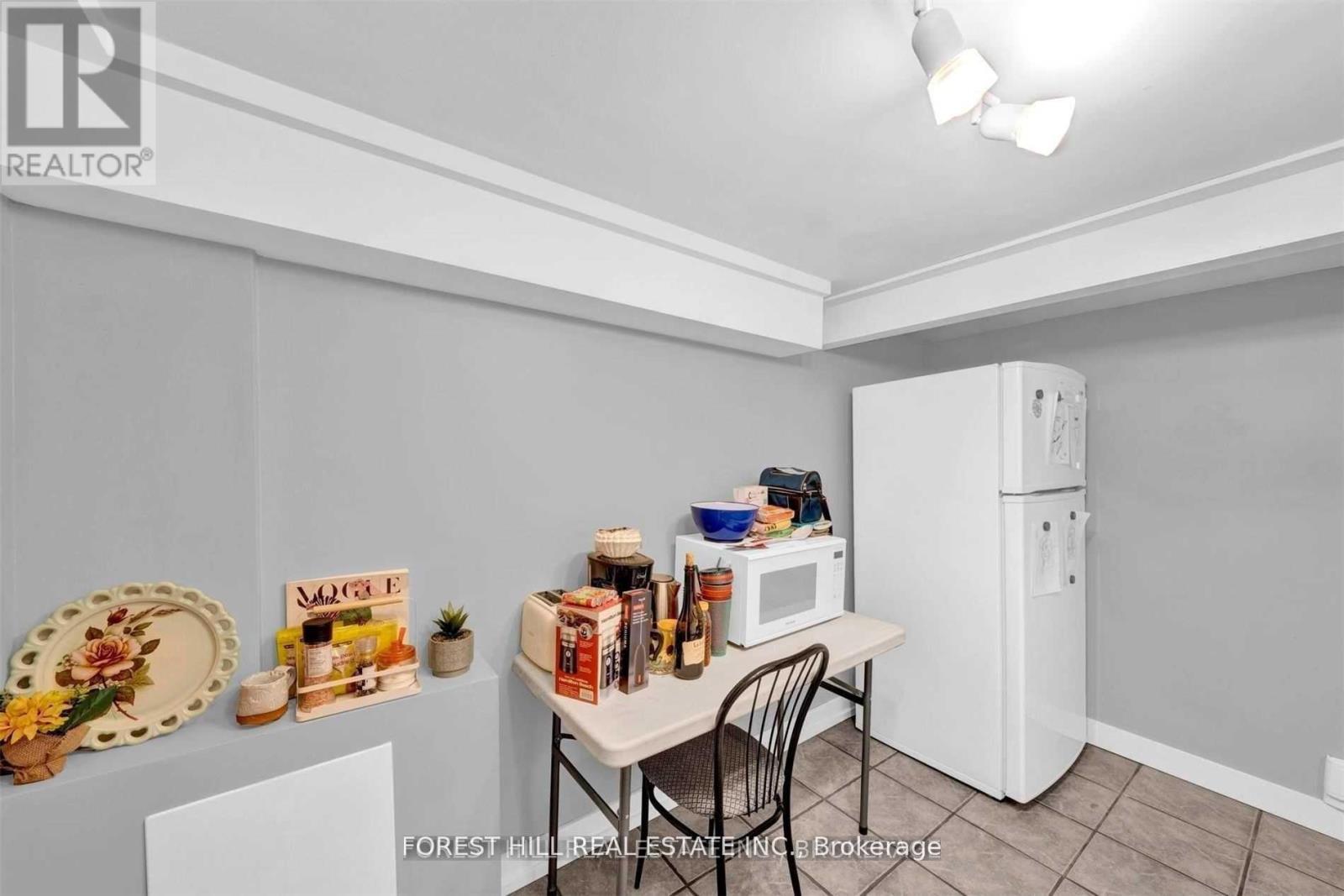 A kitchen with a white refrigerator, a table with chairs, and a bowl of fruit on the table.