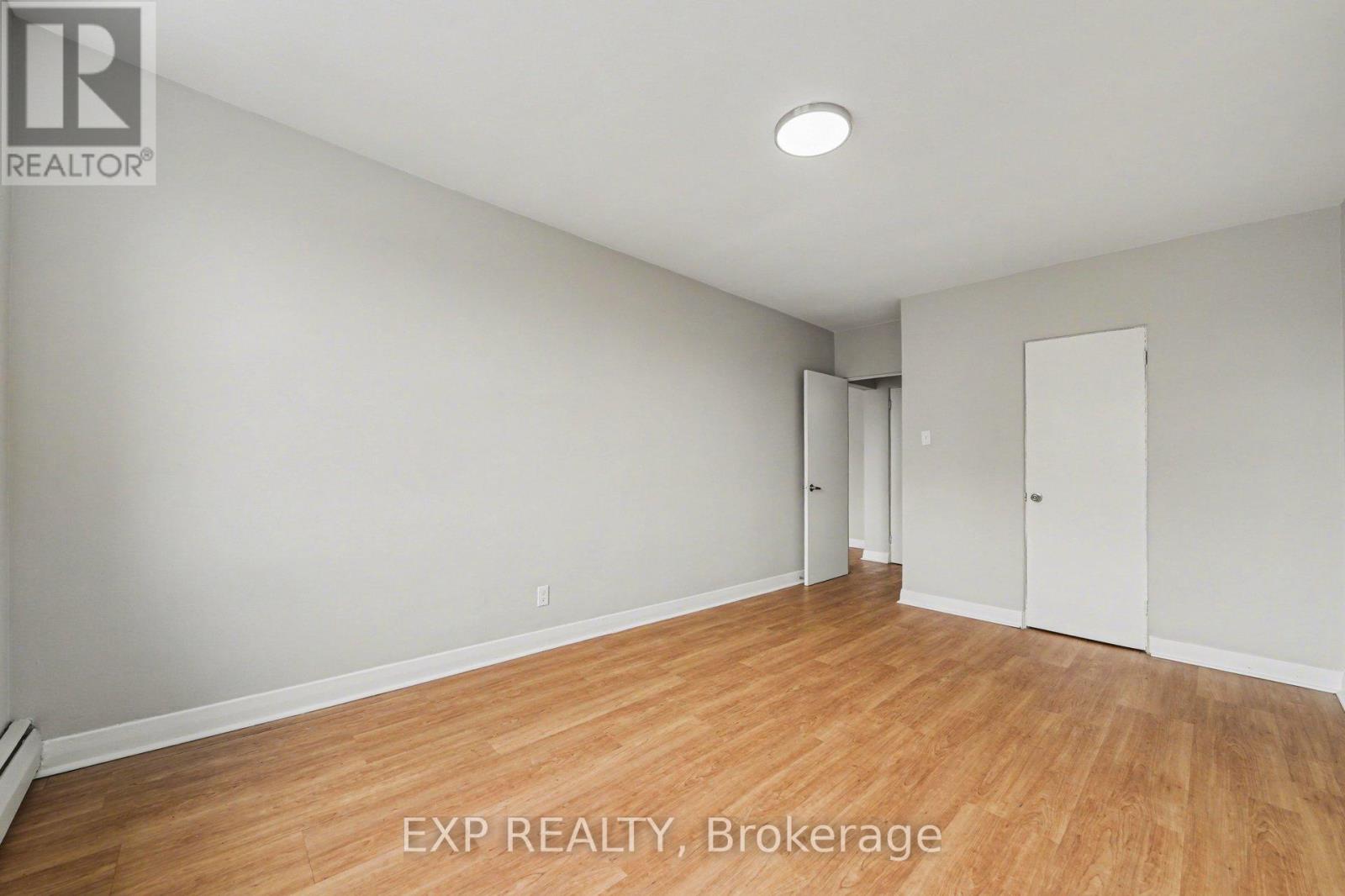 A room with wooden flooring and white walls, with a door on the right side.