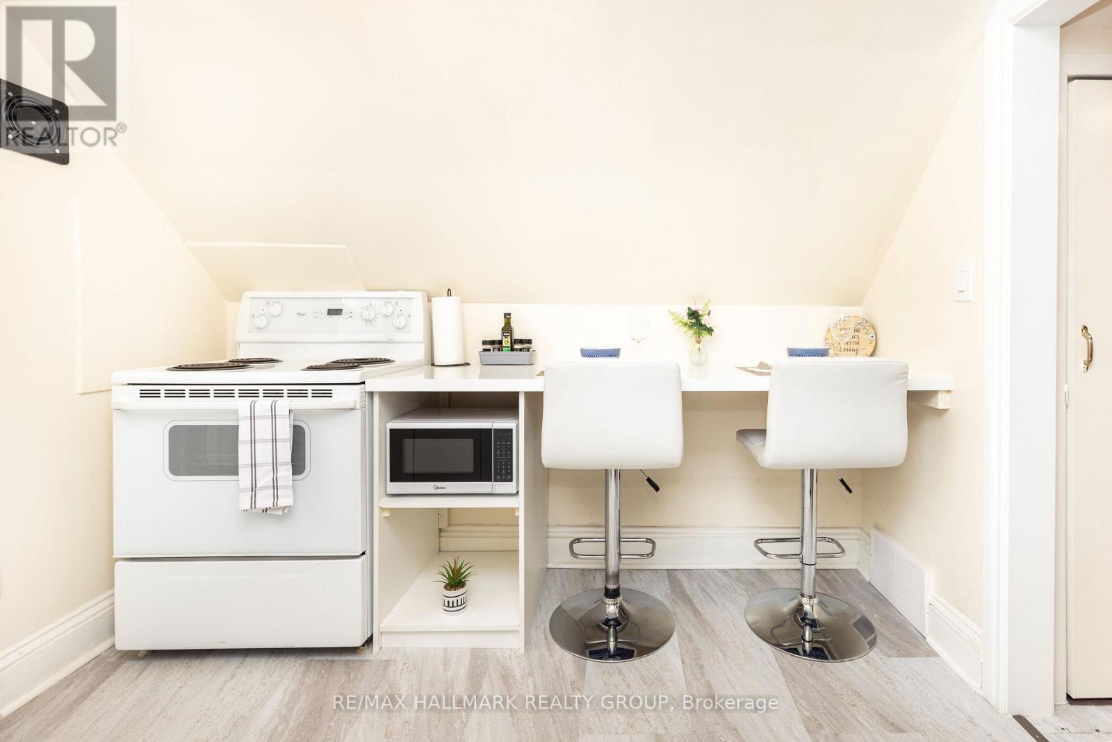 A kitchen with a white oven and microwave, a white table with two chairs, and a plant on the counter.
