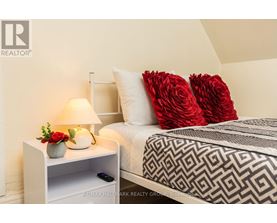 A bedroom with a bed, a nightstand with a lamp, and a vase of flowers.