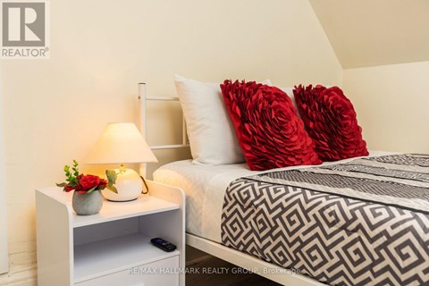 A bedroom with a bed, a nightstand with a lamp, and a vase of flowers.