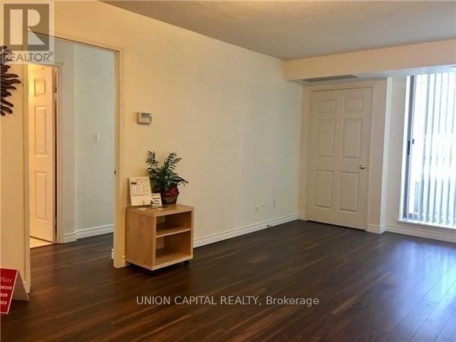 A room with wooden floors and white walls, furnished with a wooden shelf and a plant.