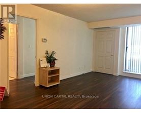 A room with wooden floors and white walls, furnished with a wooden shelf and a plant.
