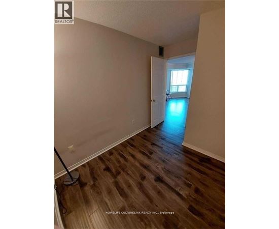 A room with wooden floors and a brokerage sign on the wall.