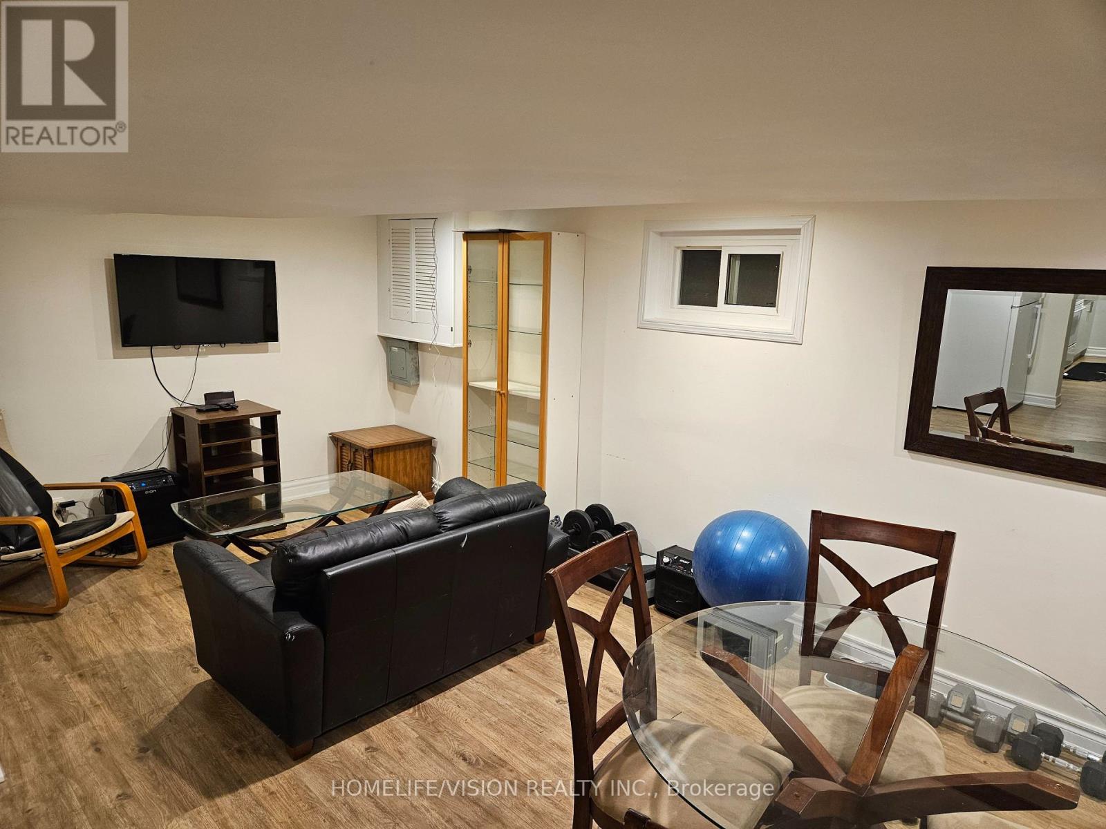 A living room with a black couch, a glass table, a TV, a mirror, and a blue exercise ball.