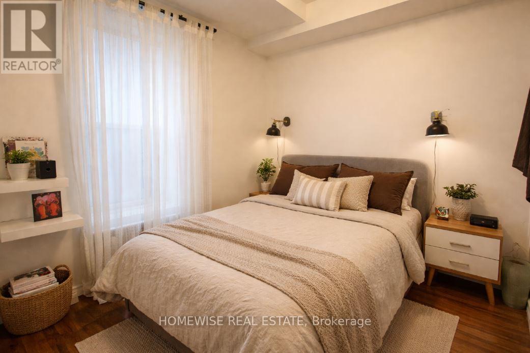 A bedroom with a large bed, a nightstand, and a window with sheer curtains.